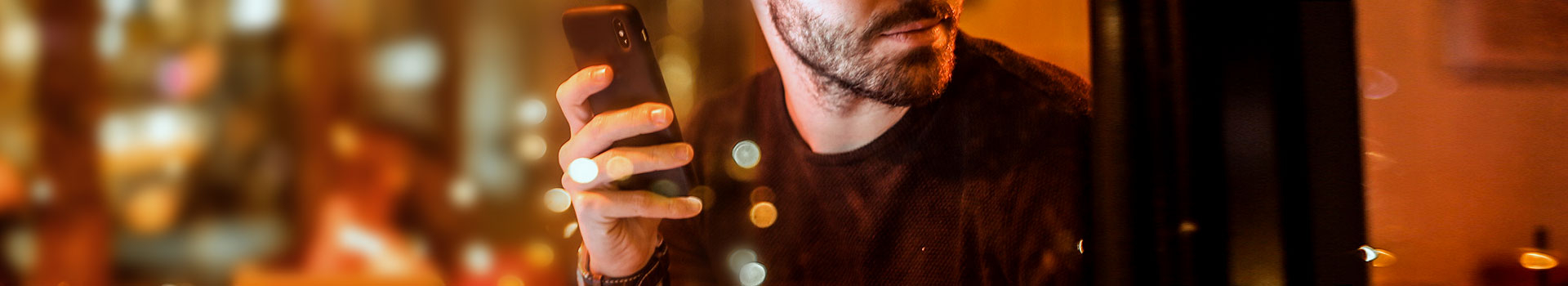 Man bekijkt wisselend op zijn smartphone en naar buiten in een sfeervolle bar